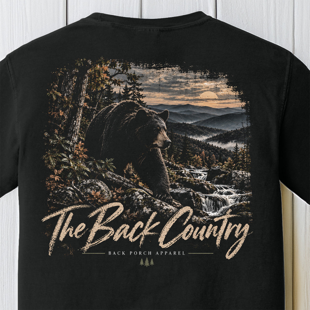 A black short-sleeve t-shirt featuring a large back graphic of a bear in a mountain landscape with the text 'The Back Country' and 'BACK PORCH APPAREL'.