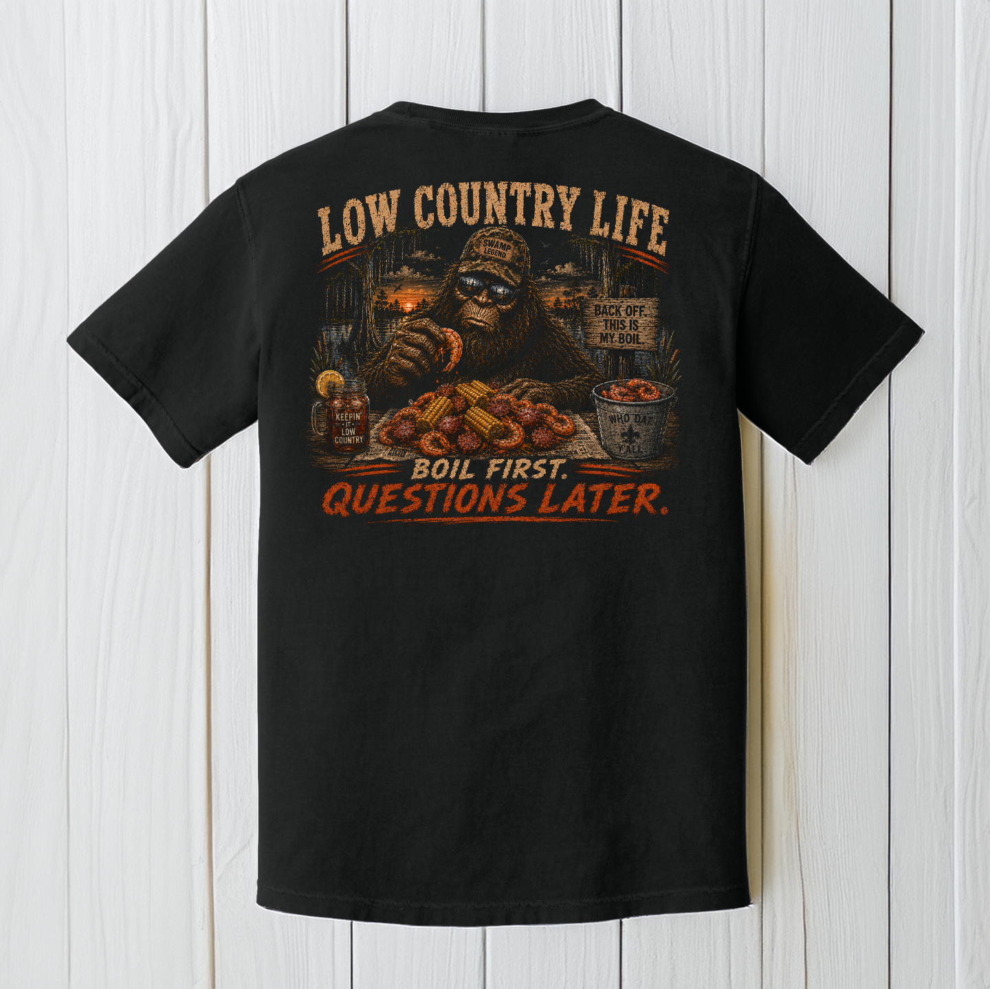 Black Comfort Colors Bigfoot crawfish boil t-shirt displayed on a white wood background featuring Low Country Life artwork.
