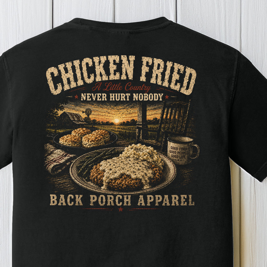 Distressed southern country graphic featuring chicken fried steak with gravy, farmhouse sunset scenery, and rustic porch artwork on a black Comfort Colors shirt.
