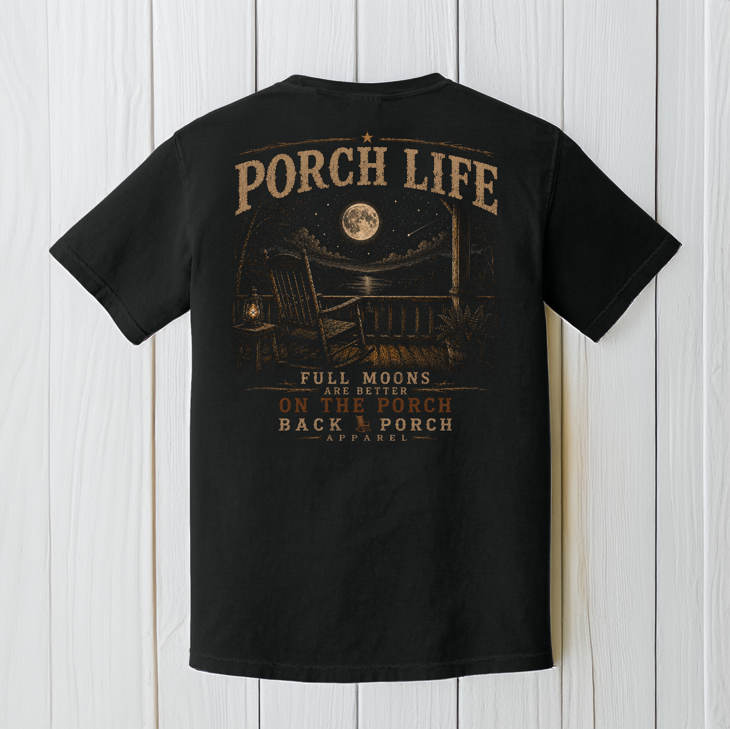 Black Comfort Colors porch life t-shirt displayed on a white wood background featuring a full moon, rocking chair, lantern, and peaceful nighttime country porch scene.