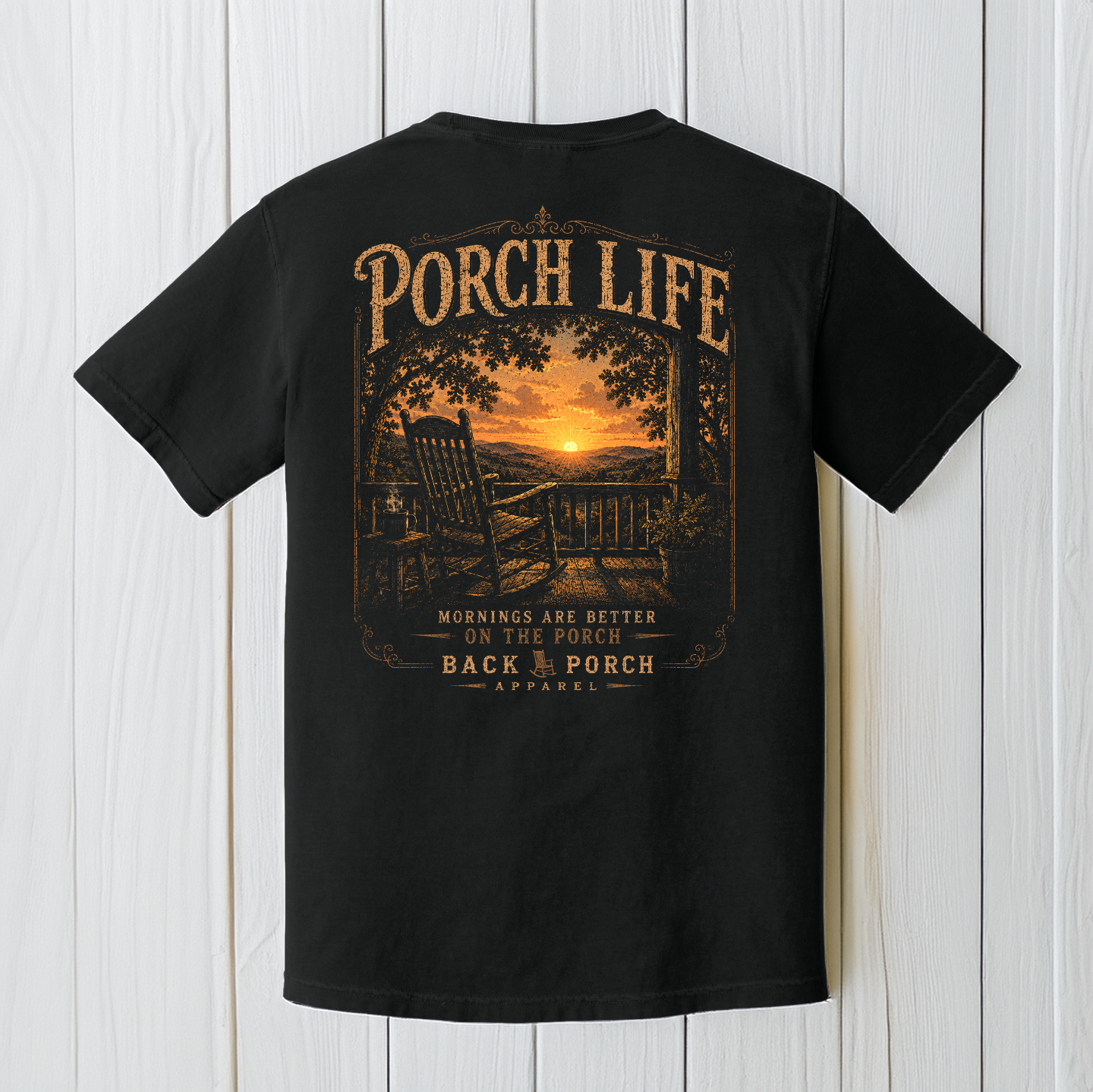 Black Comfort Colors Porch Life graphic t-shirt displayed on a white wood background featuring a peaceful country sunrise viewed from a front porch rocking chair.