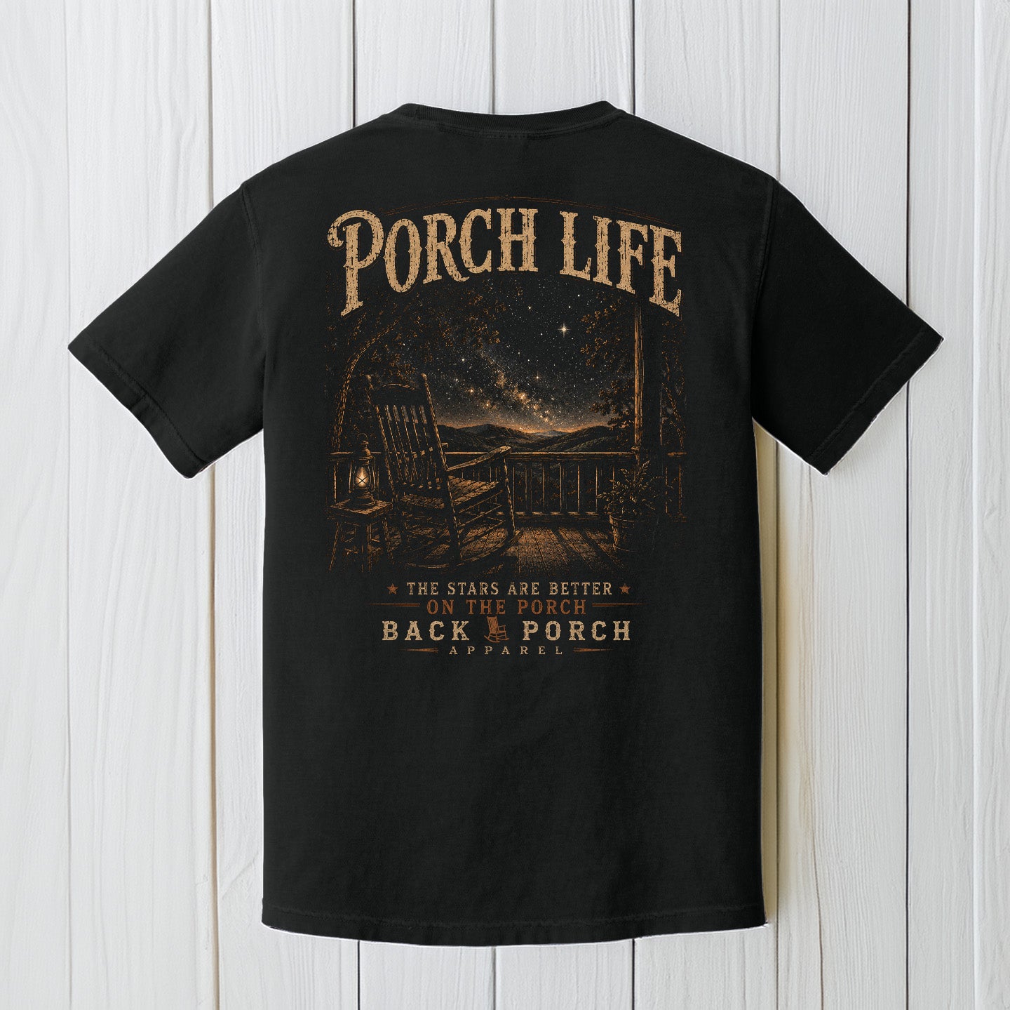 Black Comfort Colors t-shirt featuring a Porch Life nighttime mountain porch scene displayed on a white wood background.
