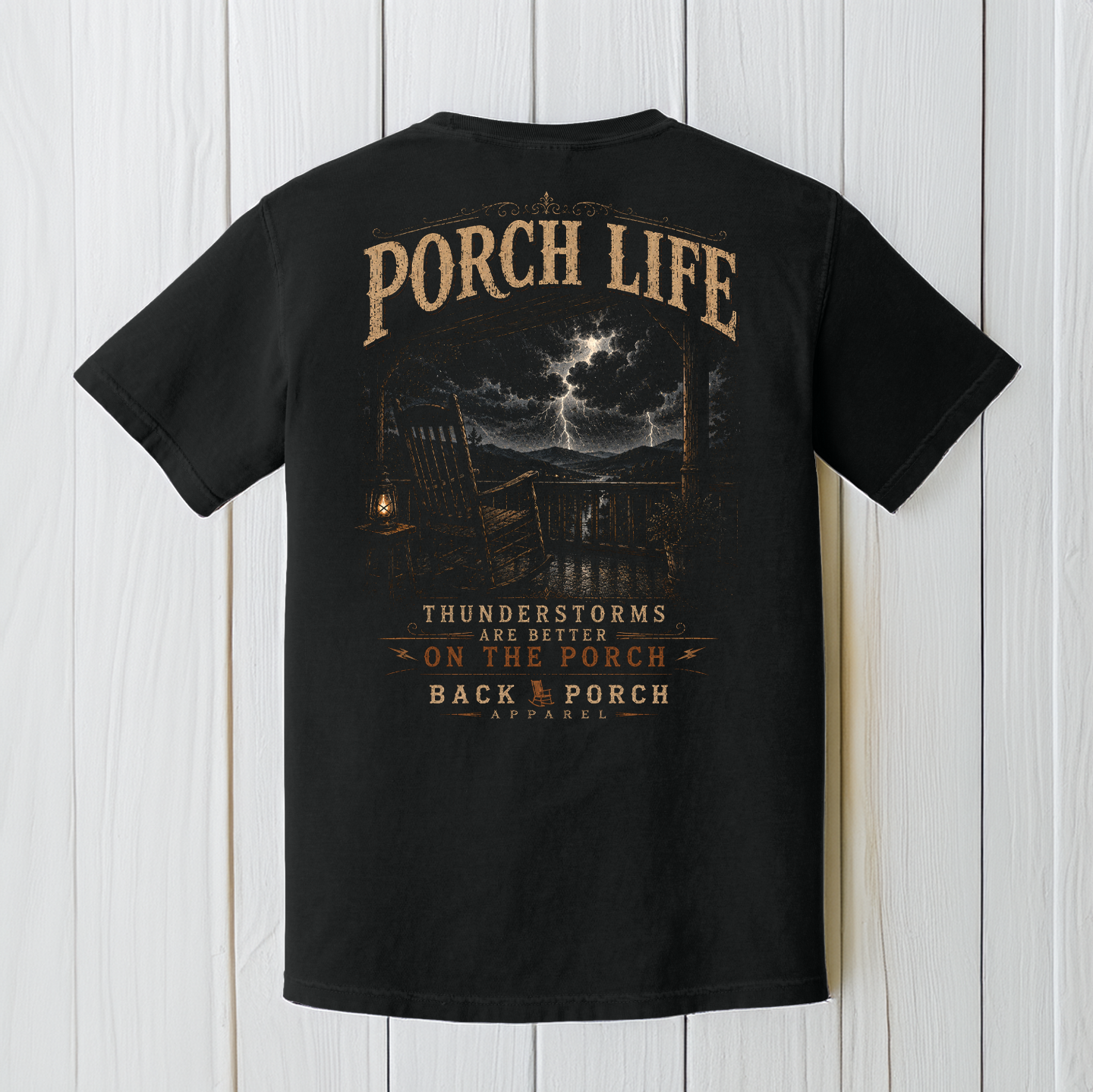Black Comfort Colors porch life t-shirt displayed on a white wood background featuring dramatic lightning, mountain scenery, rocking chair, and Thunderstorms Are Better on the Porch artwork.