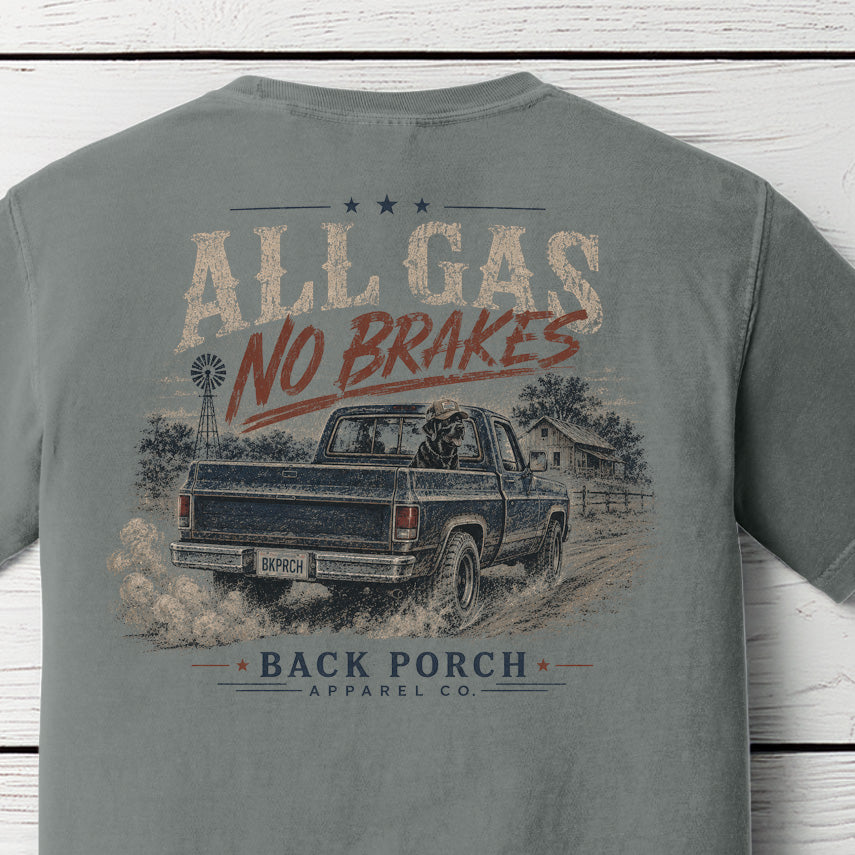 Close-up of the All Gas No Brakes graphic on a Grey Comfort Colors t-shirt showing a vintage pickup truck kicking up dust, farmhouse, windmill, and Back Porch Apparel Co. branding.