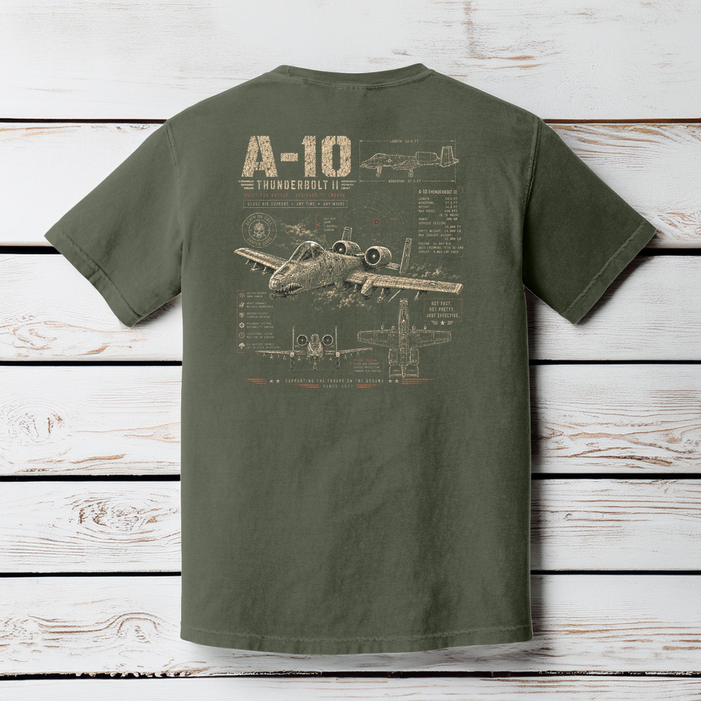 Moss Comfort Colors t-shirt hanging on a wood background featuring a distressed A-10 Thunderbolt II military aircraft schematic design.