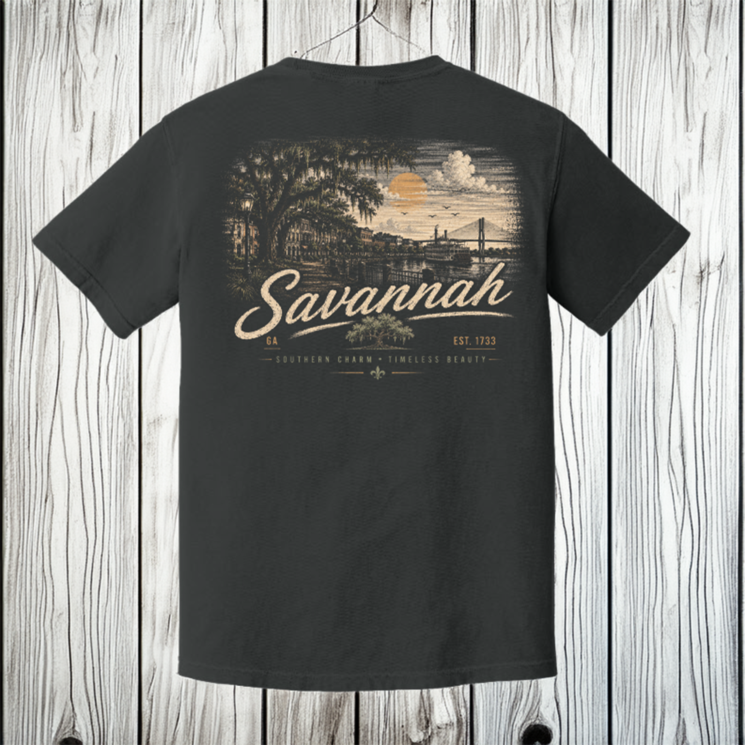 A dark charcoal gray t-shirt shown from the back, featuring a vintage-style graphic of Savannah, Georgia, with a sunset, bridge, and the word 'Savannah' in large script. The shirt is displayed hanging against a white wood plank background.