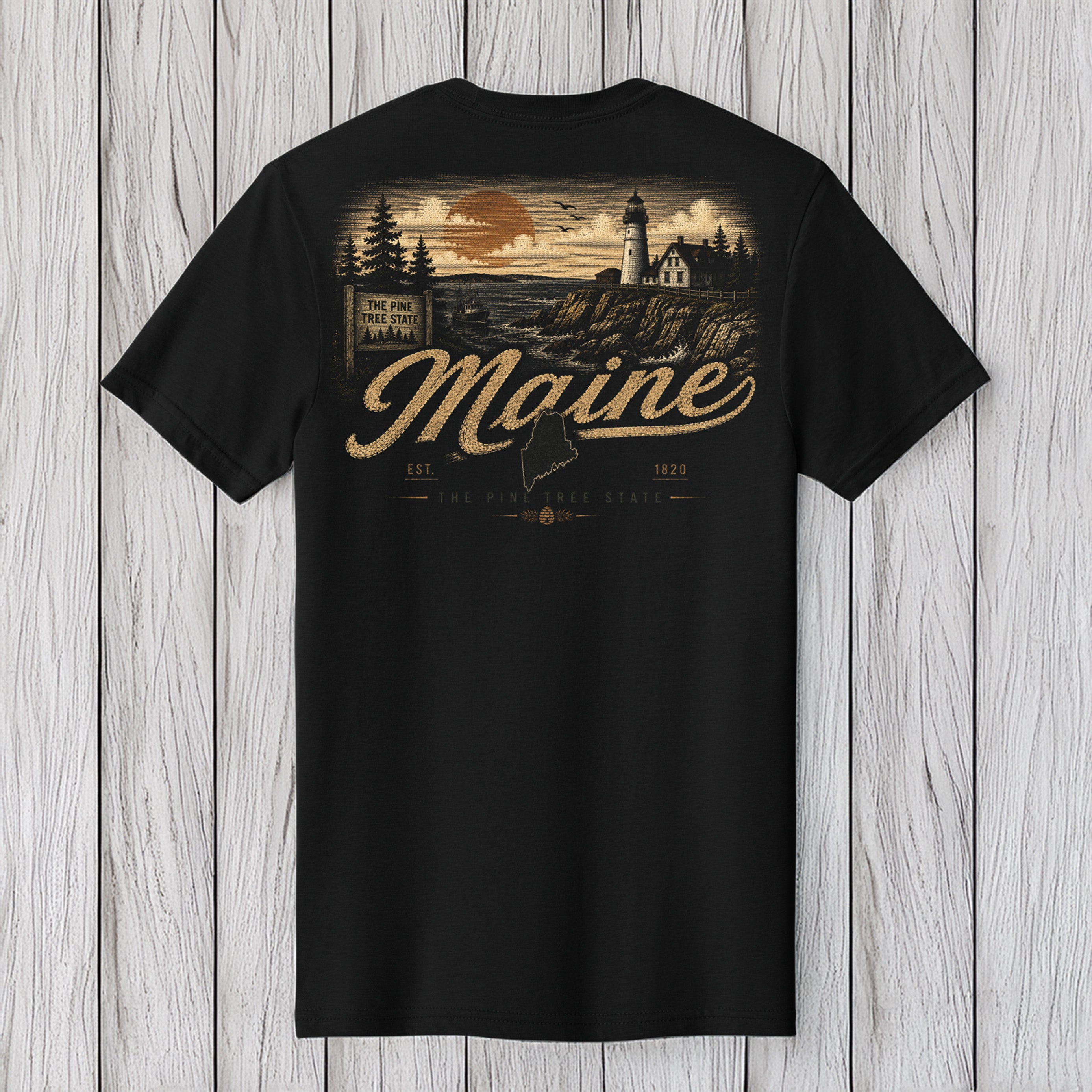 A black short-sleeve t-shirt with a vintage-style Maine graphic on the back, featuring a lighthouse, sunset, and the word 'Maine' in large script, displayed against a white wood plank background.