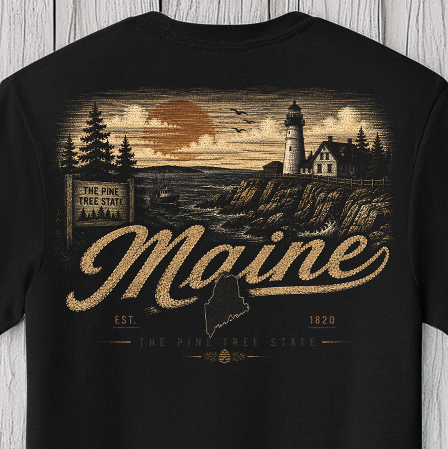 A black short-sleeve t-shirt featuring a vintage-style Maine graphic print on the front. The design includes a lighthouse, pine trees, a sunset, and the words 'Maine', 'The Pine Tree State', and 'Est.