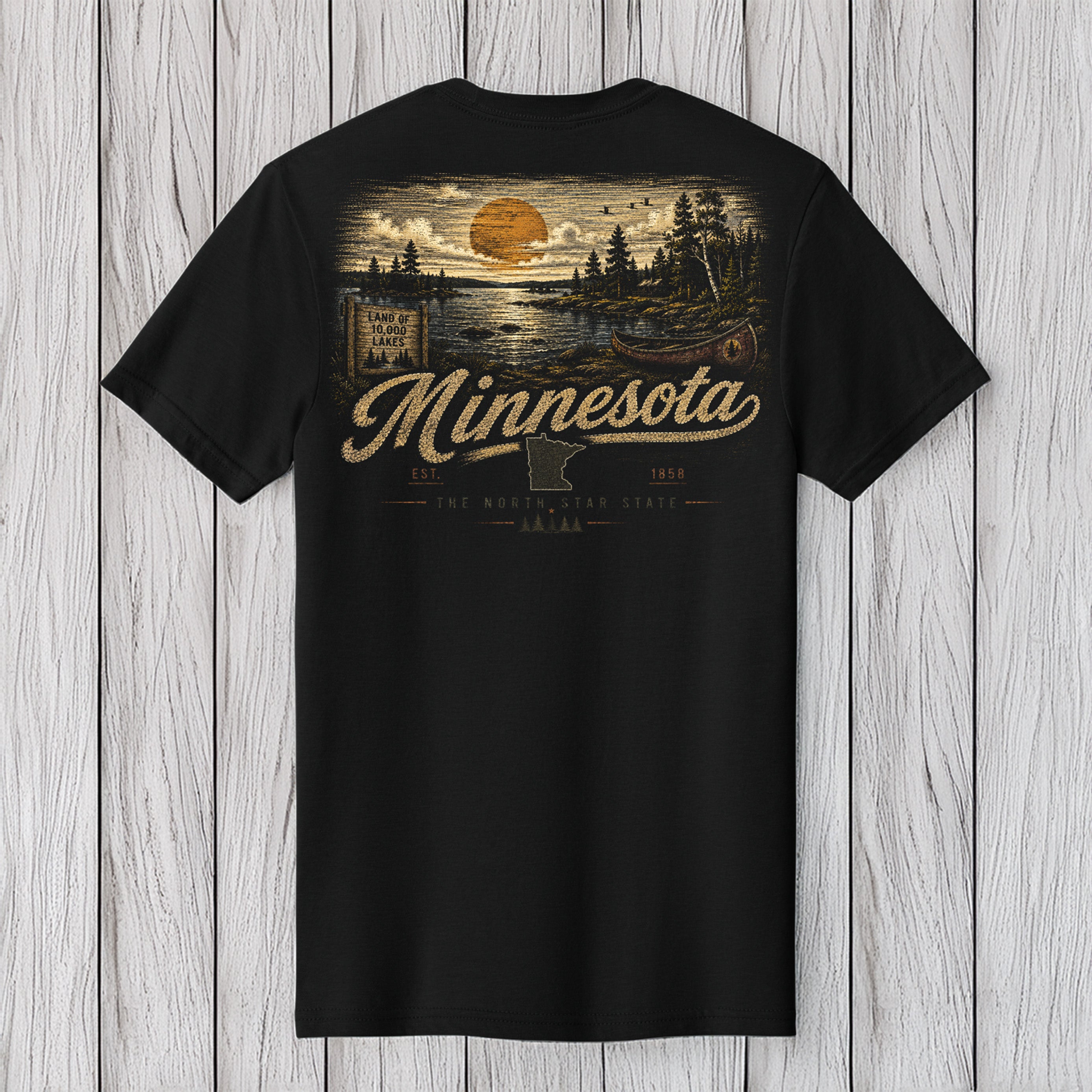 A black short-sleeve t-shirt with a vintage-style Minnesota landscape graphic on the back, featuring a sunset, trees, and the word 'Minnesota' in a cursive font, displayed against a light gray wood plank background.