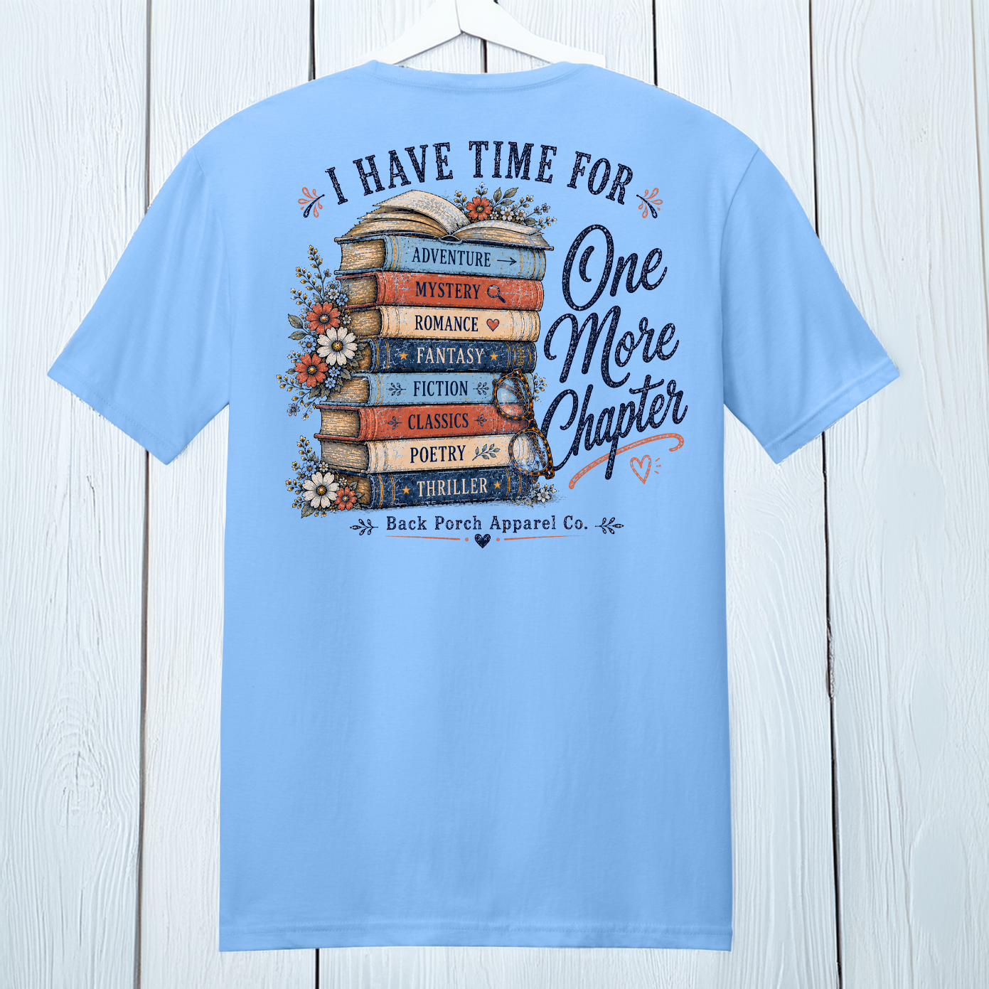 Back view of Carolina Blue One More Chapter book lover t-shirt hanging on a white wood background.