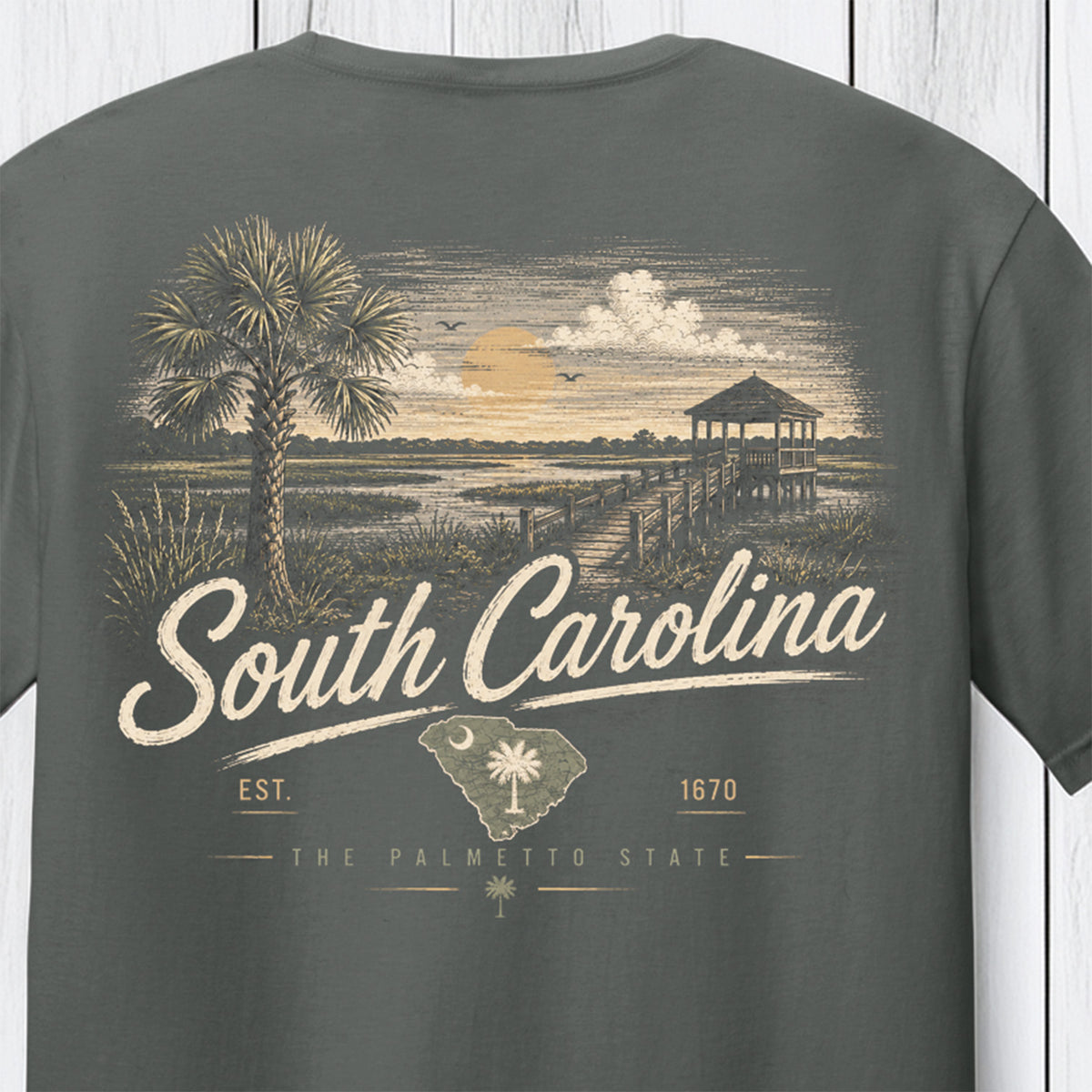 A dark gray t-shirt featuring a vintage-style South Carolina graphic print on the front, showing a palm tree, a boardwalk pier, and the text 'South Carolina' and 'The Palmetto State'.