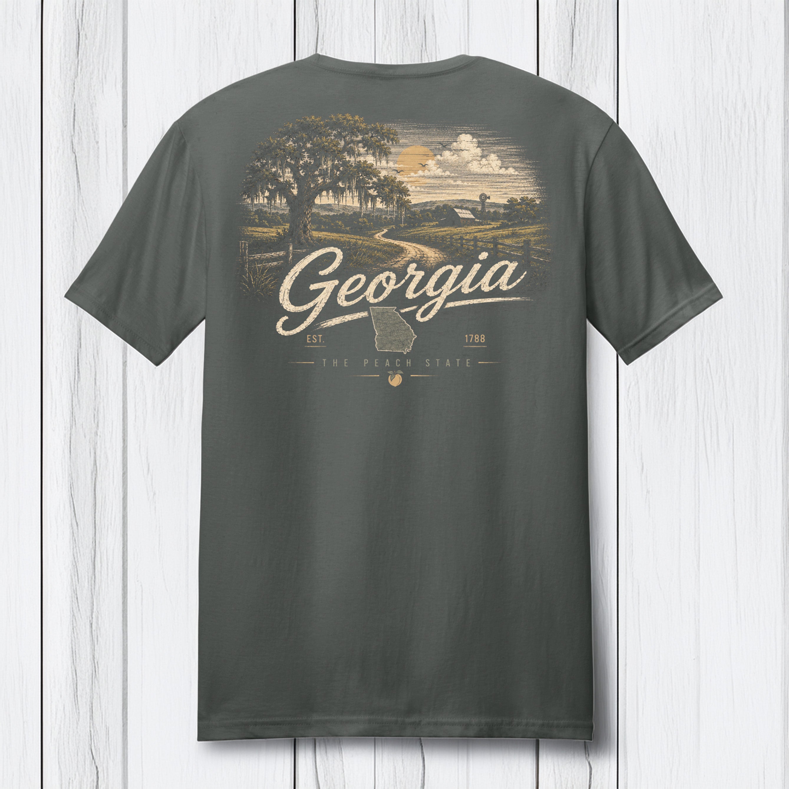 A dark gray t-shirt shown from the back, featuring a vintage-style graphic of a Georgia landscape with a tree, country road, and clouds, with 'Georgia' written in script across the center.