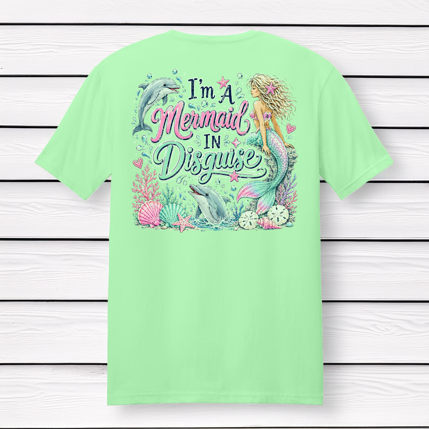 Back Porch Apparel I'm A Mermaid In Disguise short sleeve mint green t-shirt featuring a colorful mermaid, dolphins, seashells, coral, and ocean-themed back graphic.