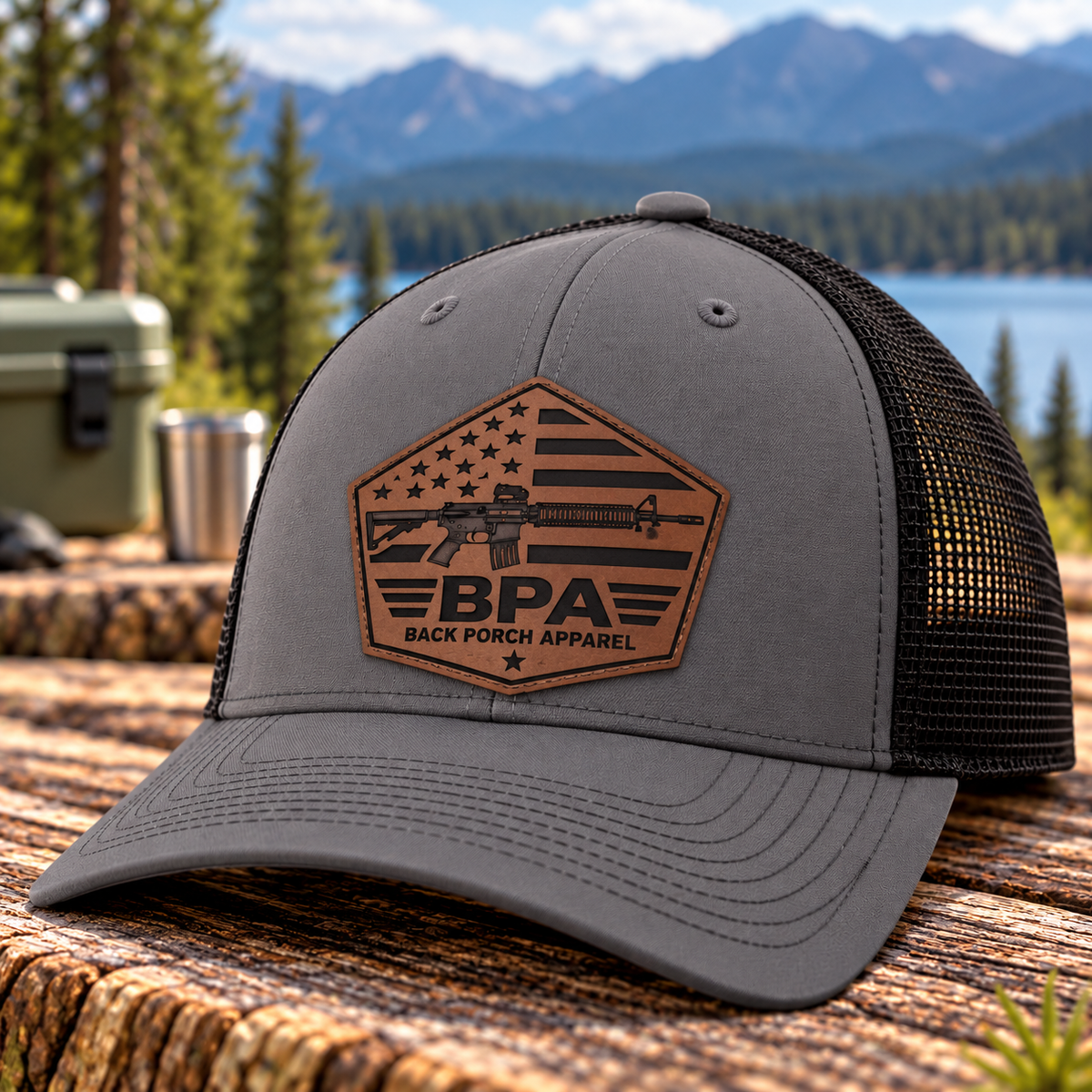 Back Porch Apparel tactical rifle and American flag dark brown leather patch on a charcoal gray and black mesh Richardson trucker hat.