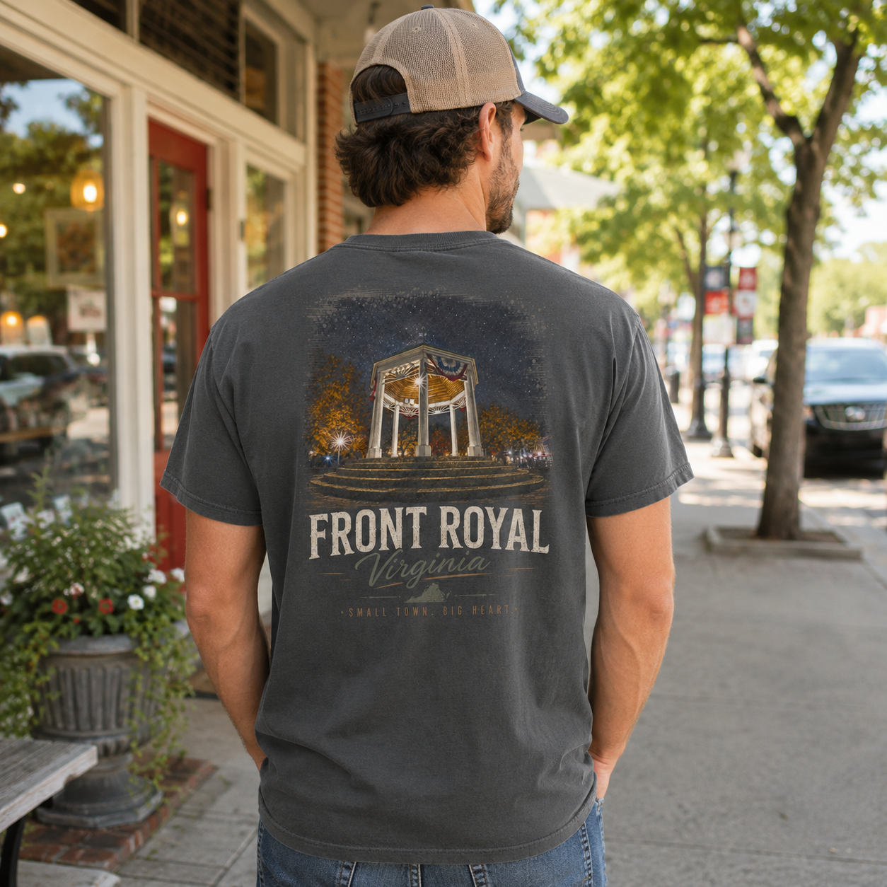 A man wearing a dark gray graphic t-shirt with a 'Front Royal Virginia' design on the back, standing on a sunny sidewalk in front of a storefront.