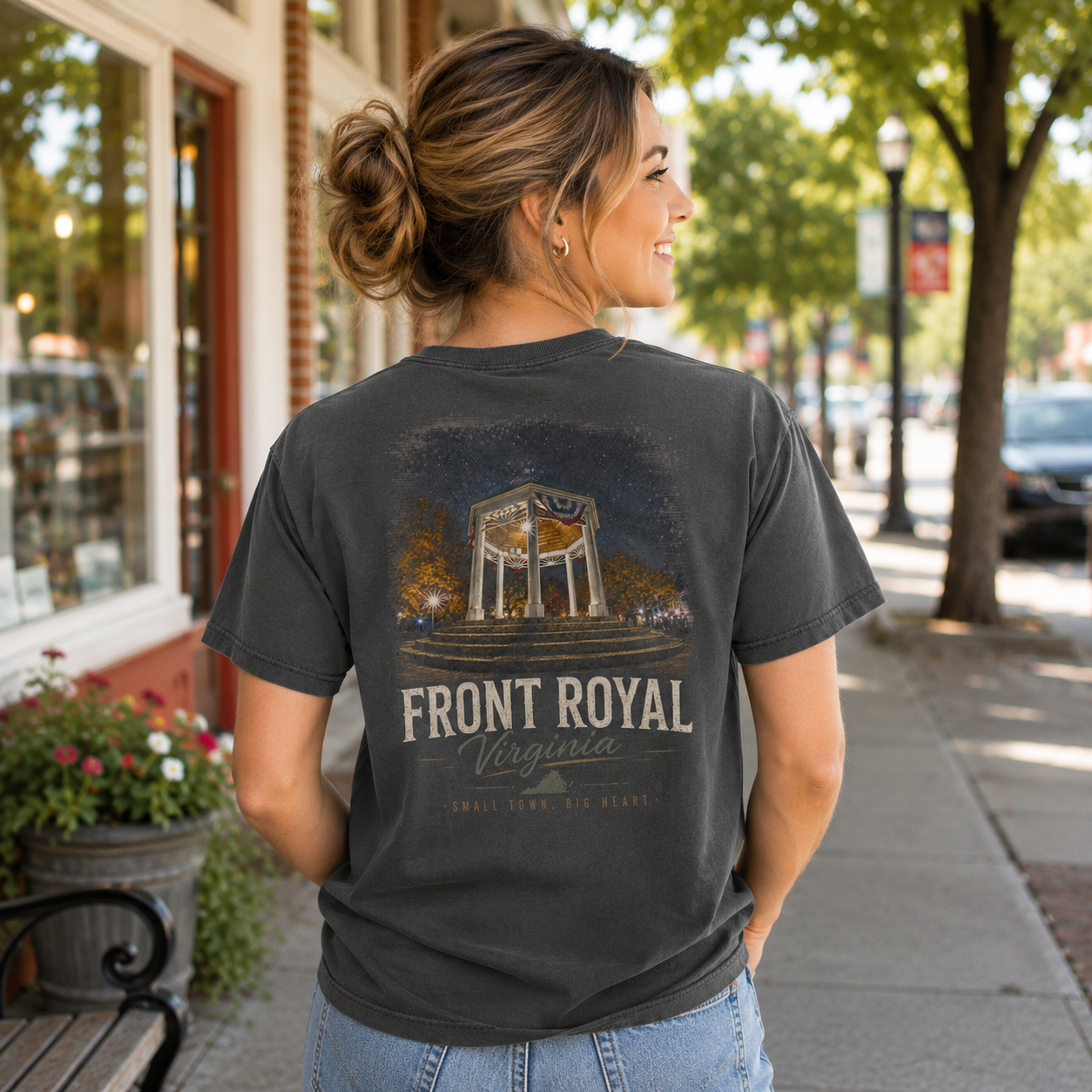 A woman stands on a city sidewalk wearing a faded charcoal gray graphic T-shirt. The back of the shirt features a distressed print of a gazebo with the text 'FRONT ROYAL Virginia' and smaller text below.