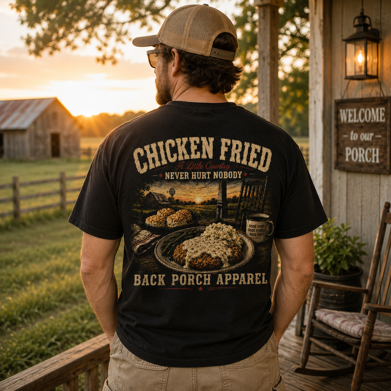 A man stands on a rustic porch at sunset wearing a black graphic T-shirt with a large chicken fried print on the back and khaki pants. The shirt reads 'CHICKEN FRIED' and 'BACK PORCH APPAREL.
