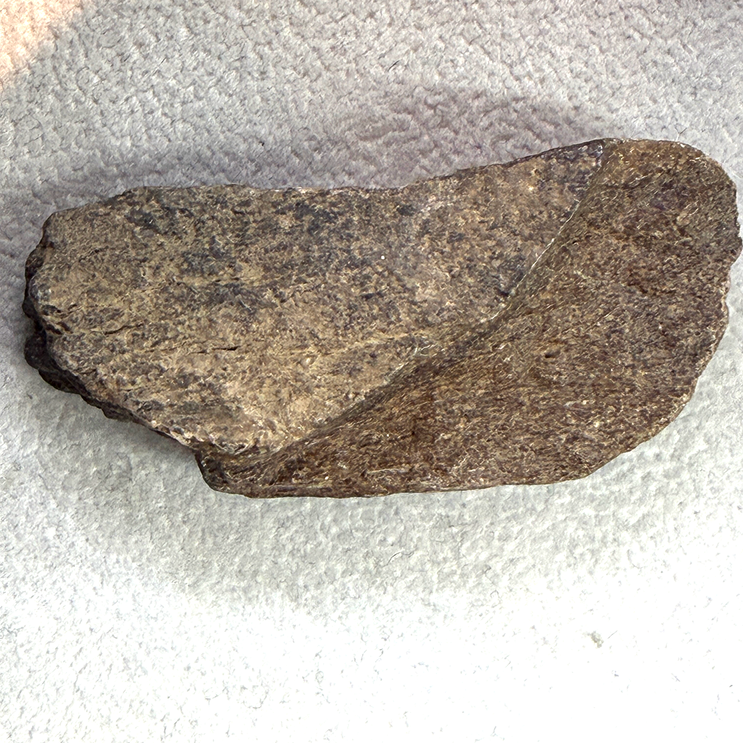 A raw, irregularly shaped stone tool or hand axe made of dark brown and gray textured stone, resting on a white textured fabric background.