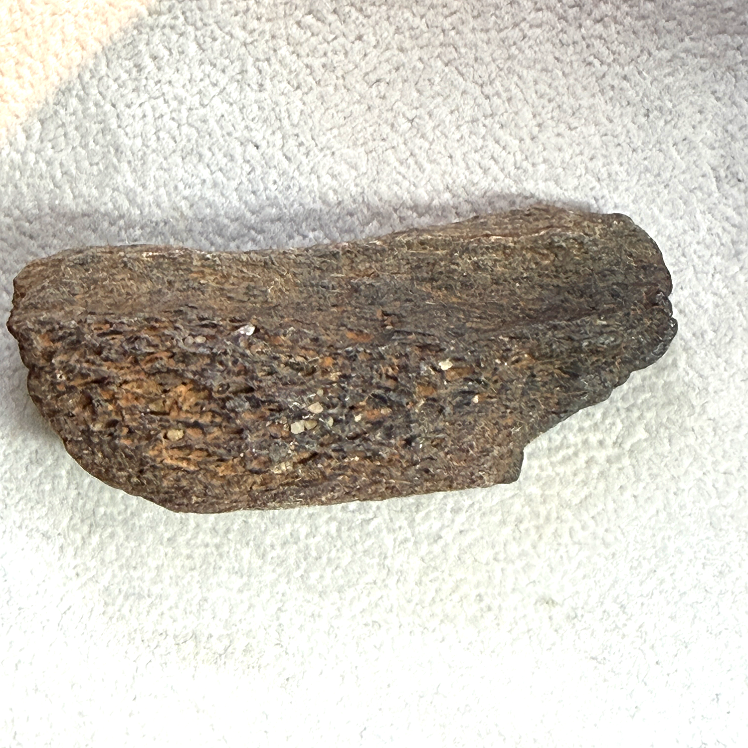 A rough, dark brown textured piece of wood or bark with natural grain, placed on a white textured fabric background.