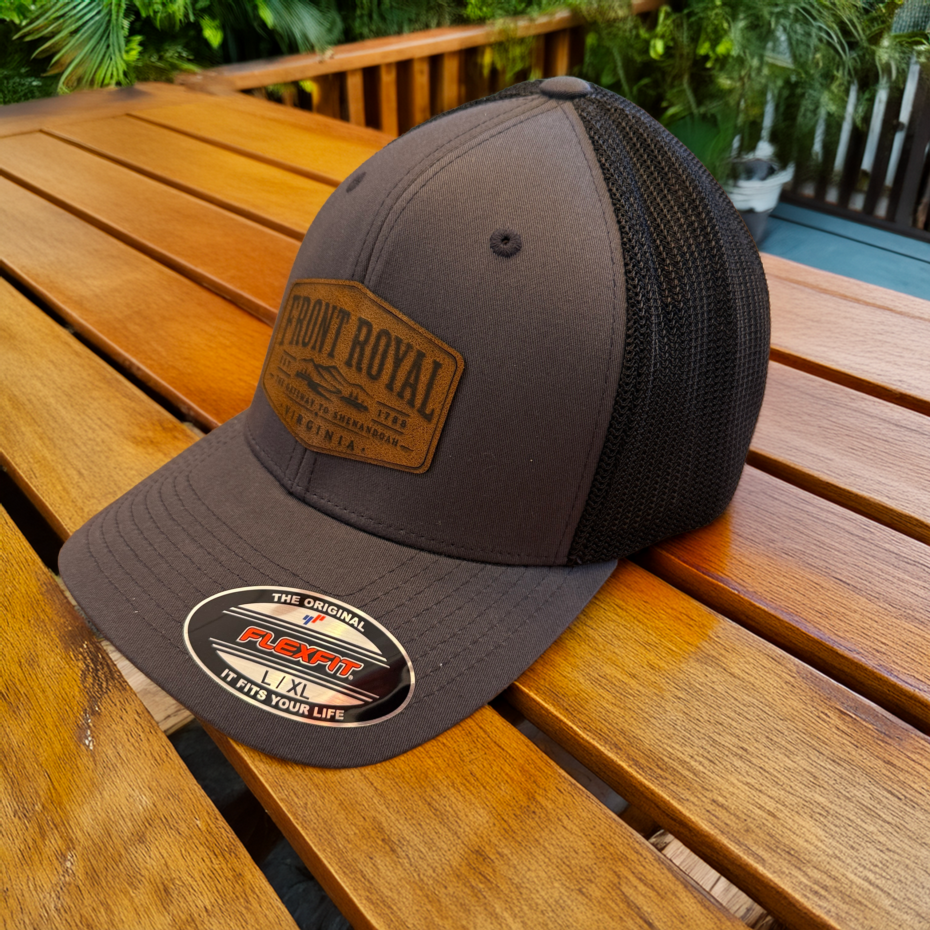 Front Royal Virginia leather patch charcoal Flexfit trucker hat displayed on a wooden outdoor table.