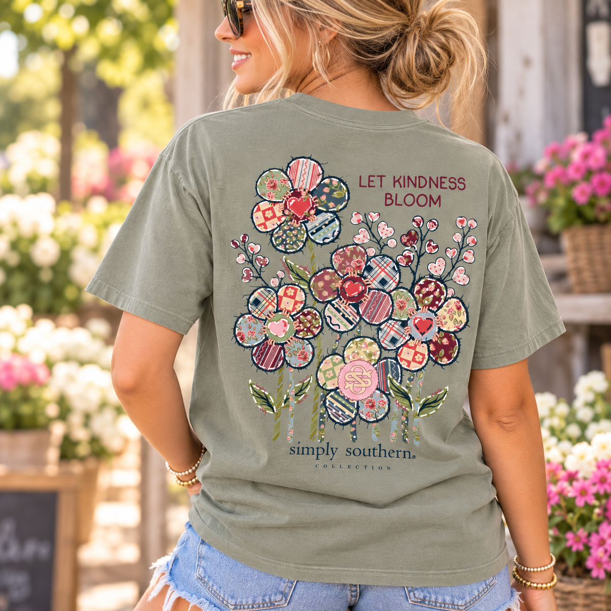 Woman wearing a Simply Southern Let Kindness Bloom mineral washed T-shirt in Birch with colorful patchwork flowers and an inspirational message on the back in a sunny garden setting.