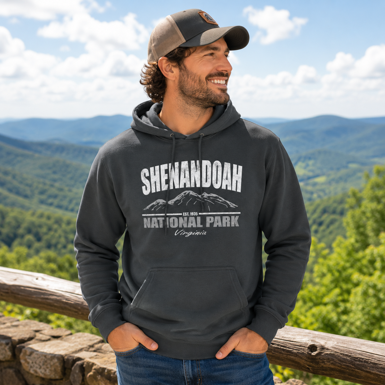 A man wearing a dark gray hoodie with a 'Shenandoah National Park' graphic, standing outdoors in front of a scenic mountain landscape.