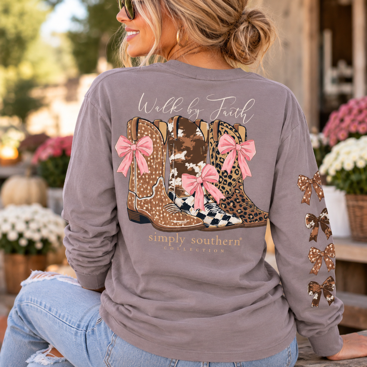 Woman wearing Simply Southern Walk by Faith western long sleeve shirt featuring patterned cowboy boots, pink bows and decorative sleeve graphics.