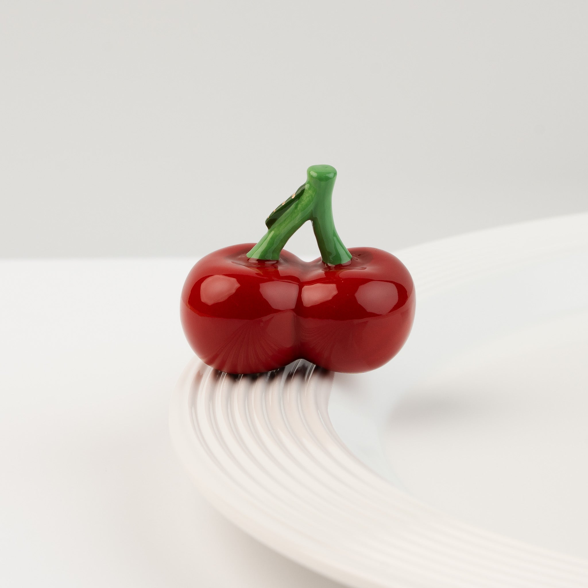 Nora Fleming Cheery Cherries Mini featuring a pair of glossy hand-painted cherries displayed on a white serving piece