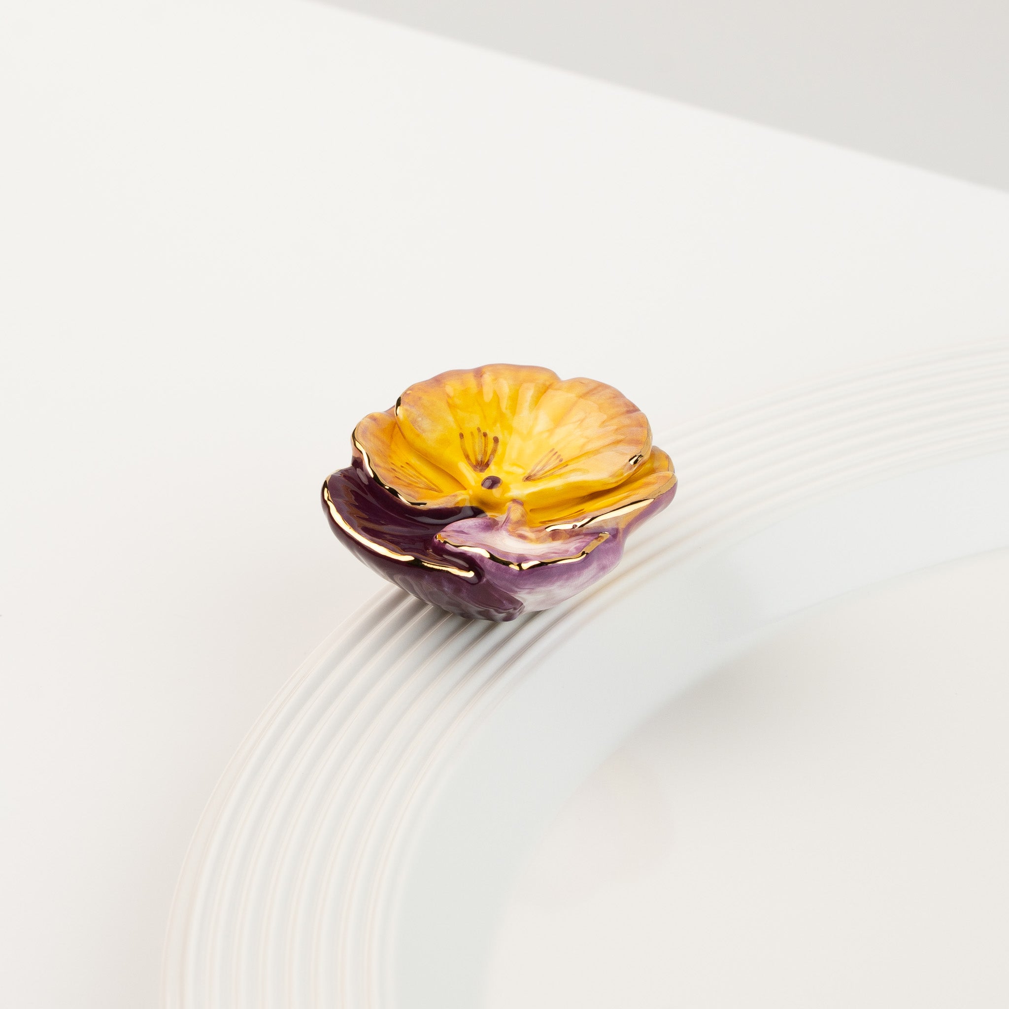 Nora Fleming Pansy Pop Mini featuring a vibrant hand-painted pansy flower displayed on a white serving piece
