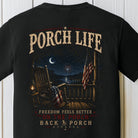 Patriotic porch graphic featuring rocking chairs, fireworks, American flags, and a nighttime lake view on a black Comfort Colors shirt.