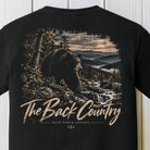 A black short-sleeve t-shirt featuring a large back graphic of a bear in a mountain landscape with the text 'The Back Country' and 'BACK PORCH APPAREL'.