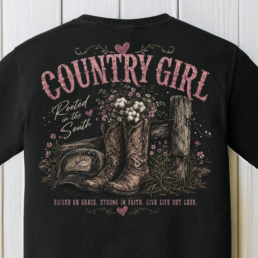 Distressed country girl graphic featuring western cowboy boots, wildflowers, rustic fence artwork, and pink southern typography on a Comfort Colors black shirt.