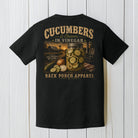 Black Comfort Colors t-shirt displayed on a wood background featuring southern cucumbers and onions in vinegar artwork with rustic farmhouse porch graphics.