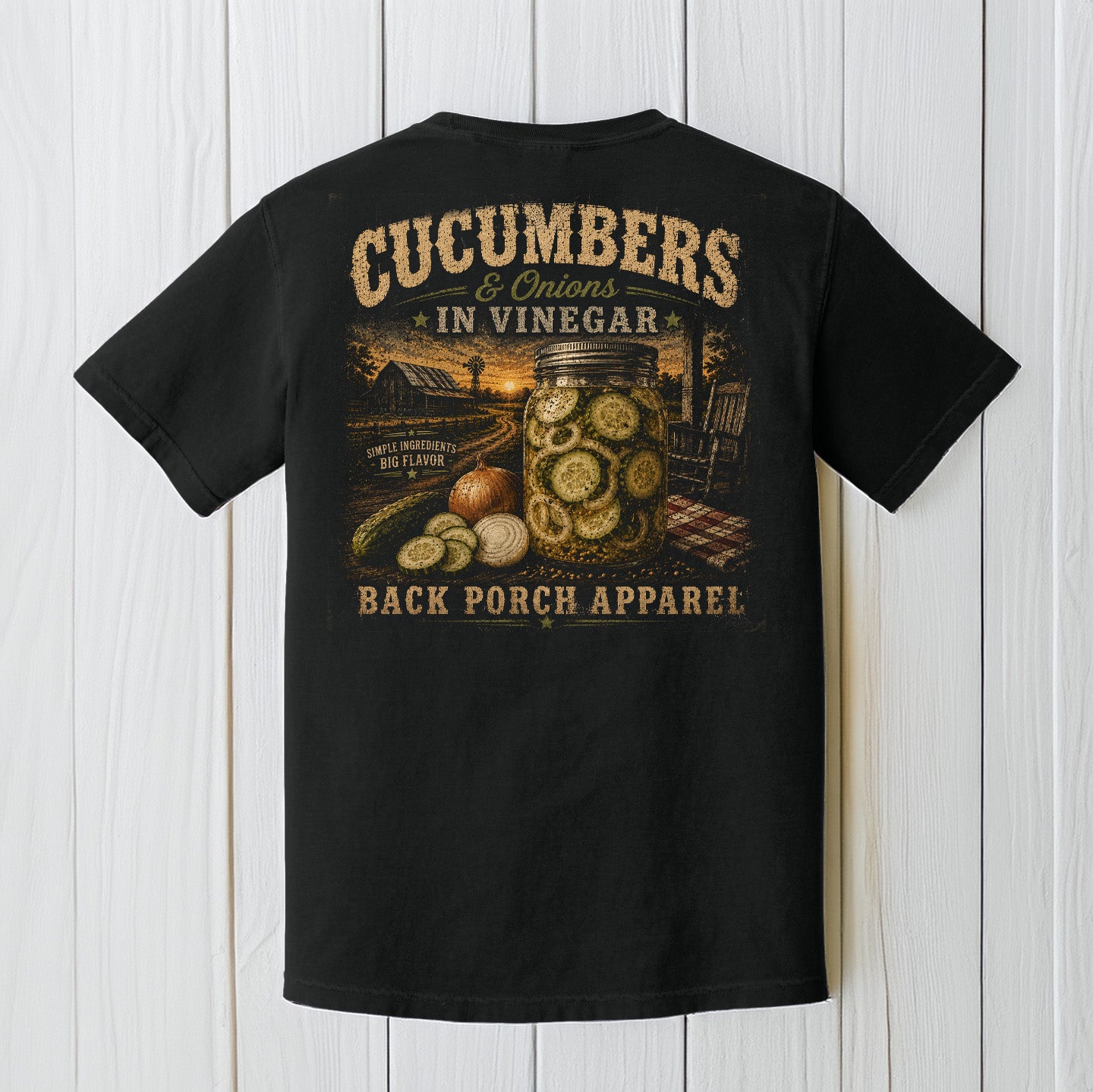 Black Comfort Colors t-shirt displayed on a wood background featuring southern cucumbers and onions in vinegar artwork with rustic farmhouse porch graphics.