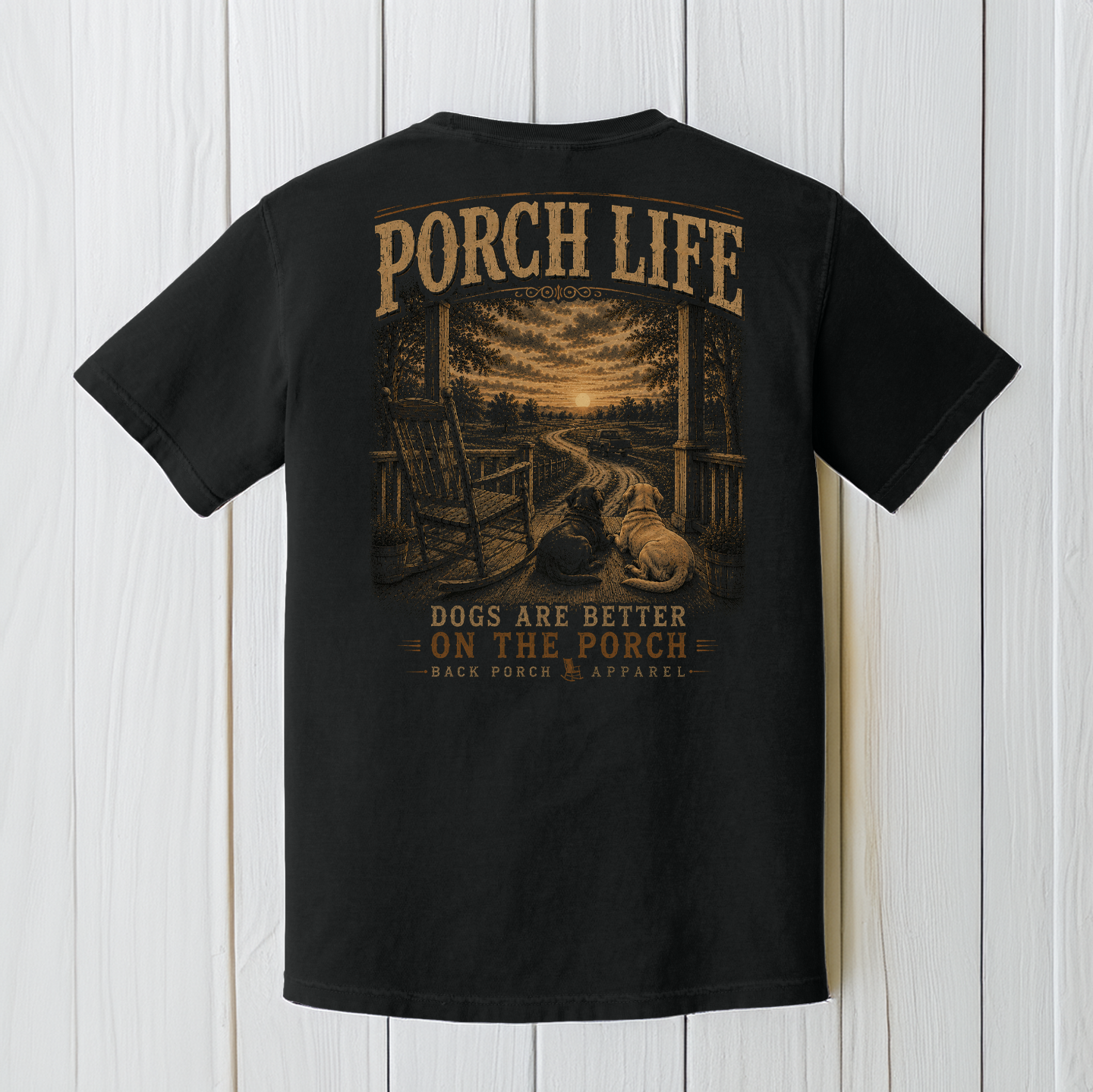 Black Comfort Colors dog lover graphic t-shirt displayed on a white wood background featuring two dogs overlooking a country sunset from a front porch.