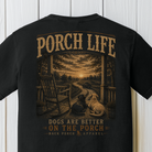 Close-up of the Porch Life Dogs Are Better on the Porch artwork showing two dogs, a rocking chair, winding country road, and sunset on a Black Comfort Colors t-shirt.
