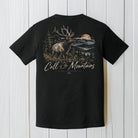 A black short-sleeve t-shirt shown from the back, featuring a large graphic print of a moose in a mountain landscape with the text 'Call of The Mountains' and 'Rocky Mountain National Park' on a white wood plank background.