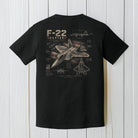 Black Comfort Colors F-22 Raptor t-shirt displayed on a white wood background.