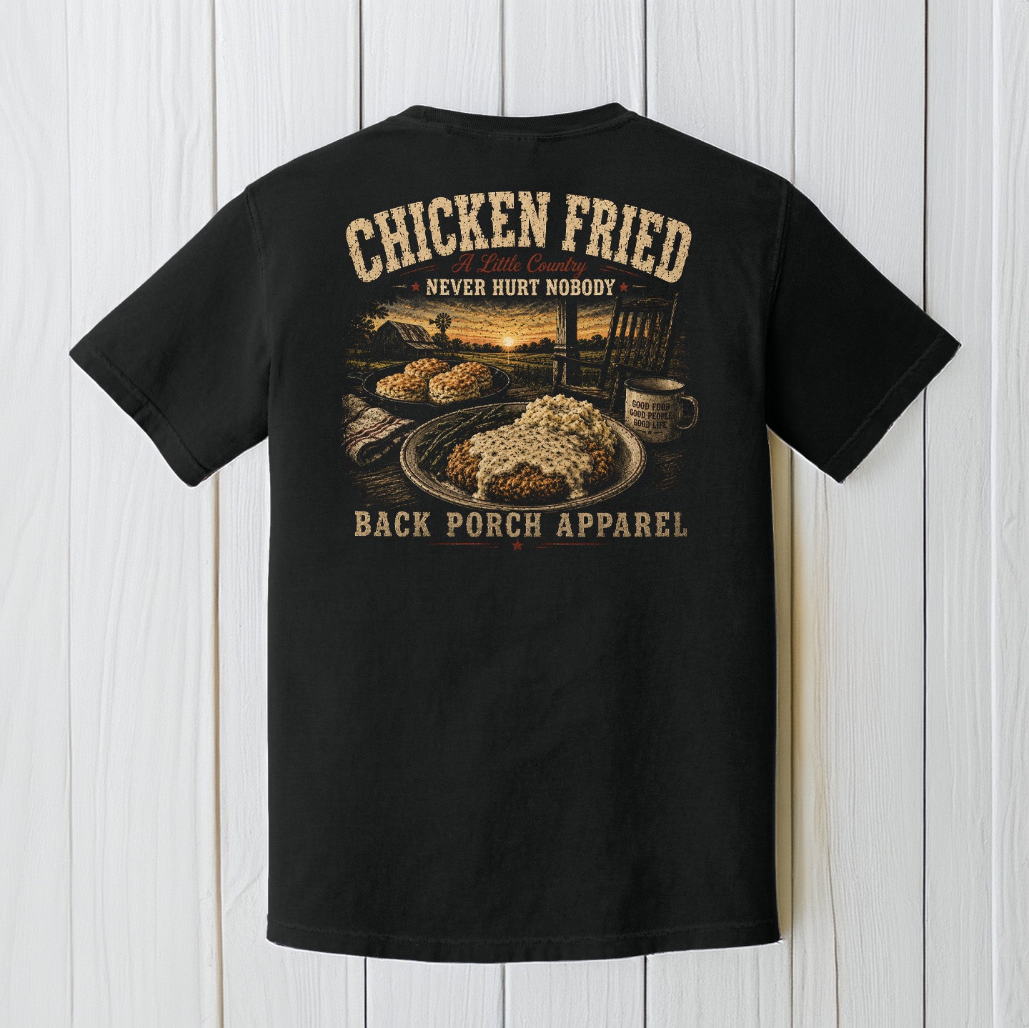 Black Comfort Colors t-shirt displayed on a wood background featuring a southern chicken fried steak graphic with rustic farmhouse porch artwork.