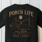 Close-up of the Porch Life Full Moons Are Better on the Porch artwork showing a rocking chair, glowing lantern, full moon, and rustic nighttime porch on a Black Comfort Colors t-shirt.