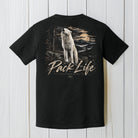 A black short-sleeve t-shirt shown from the back, featuring a large graphic print of a howling wolf in a forest at sunset with the text 'Pack Life' and '4x4 POWER MEASURES'. The shirt is displayed flat against a white vertical wood plank background.