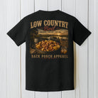 Black Comfort Colors t-shirt displayed on a wood background featuring a low country boil seafood graphic with rustic coastal southern artwork.