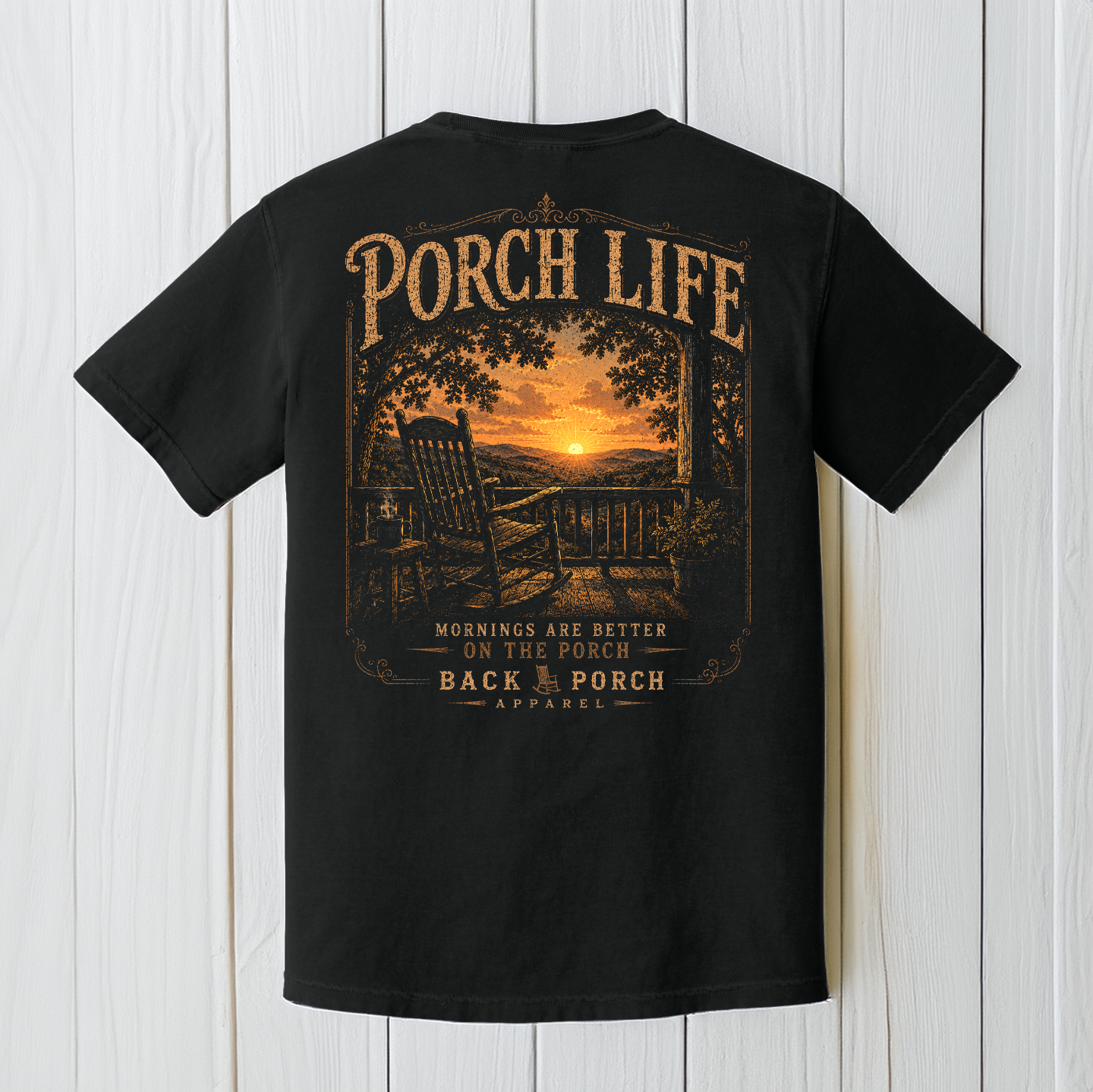 Black Comfort Colors Porch Life graphic t-shirt displayed on a white wood background featuring a peaceful country sunrise viewed from a front porch rocking chair.