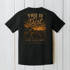 Black Comfort Colors t-shirt displayed on a wood background featuring a rustic country farm tractor graphic with sunset scenery.