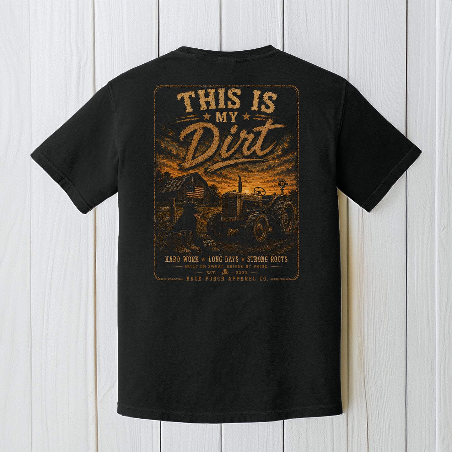 Black Comfort Colors t-shirt displayed on a wood background featuring a rustic country farm tractor graphic with sunset scenery.