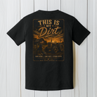 Black Comfort Colors t-shirt with a large distressed farm scene graphic on the back featuring a tractor, barn, sunset sky, and “This Is My Dirt” country slogan.