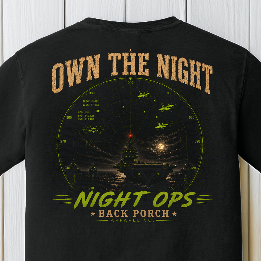 Close-up of the Own the Night Night Ops artwork showing a moonlit aircraft carrier, radar display, and fighter aircraft on a Black Comfort Colors t-shirt.