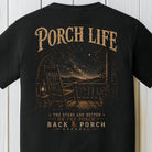 Rustic nighttime porch graphic with rocking chair, lantern, mountains, and star-filled sky on a black Comfort Colors shirt.