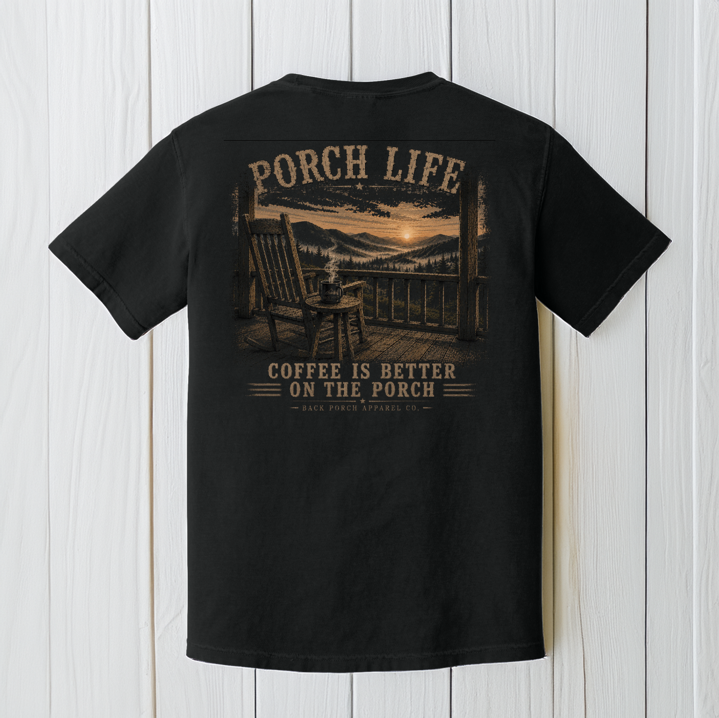 Black Comfort Colors porch life t-shirt displayed on a white wood background featuring a mountain sunrise, rocking chair, and coffee mug with Coffee Is Better on the Porch artwork.