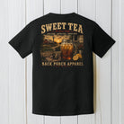 Black Comfort Colors t-shirt hanging on a wood background featuring a vintage sweet tea porch life graphic with mason jar and southern farmhouse artwork.